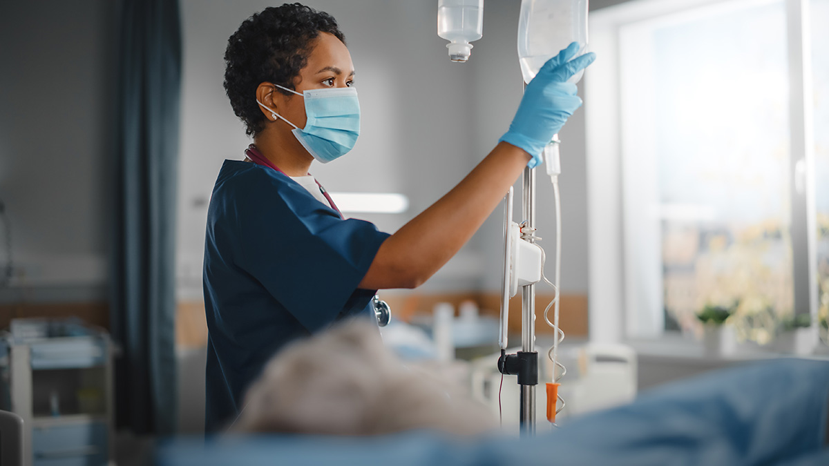Nurse checks the IV bag over a palliative care cancer patient.