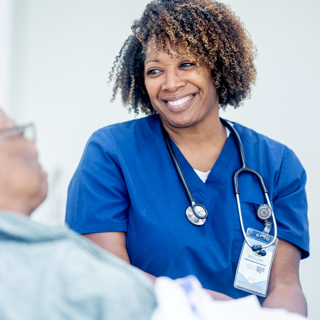 A nurse in scrubs talks with a patient, providing compassionate cancer inpatient care in a bright clinical room