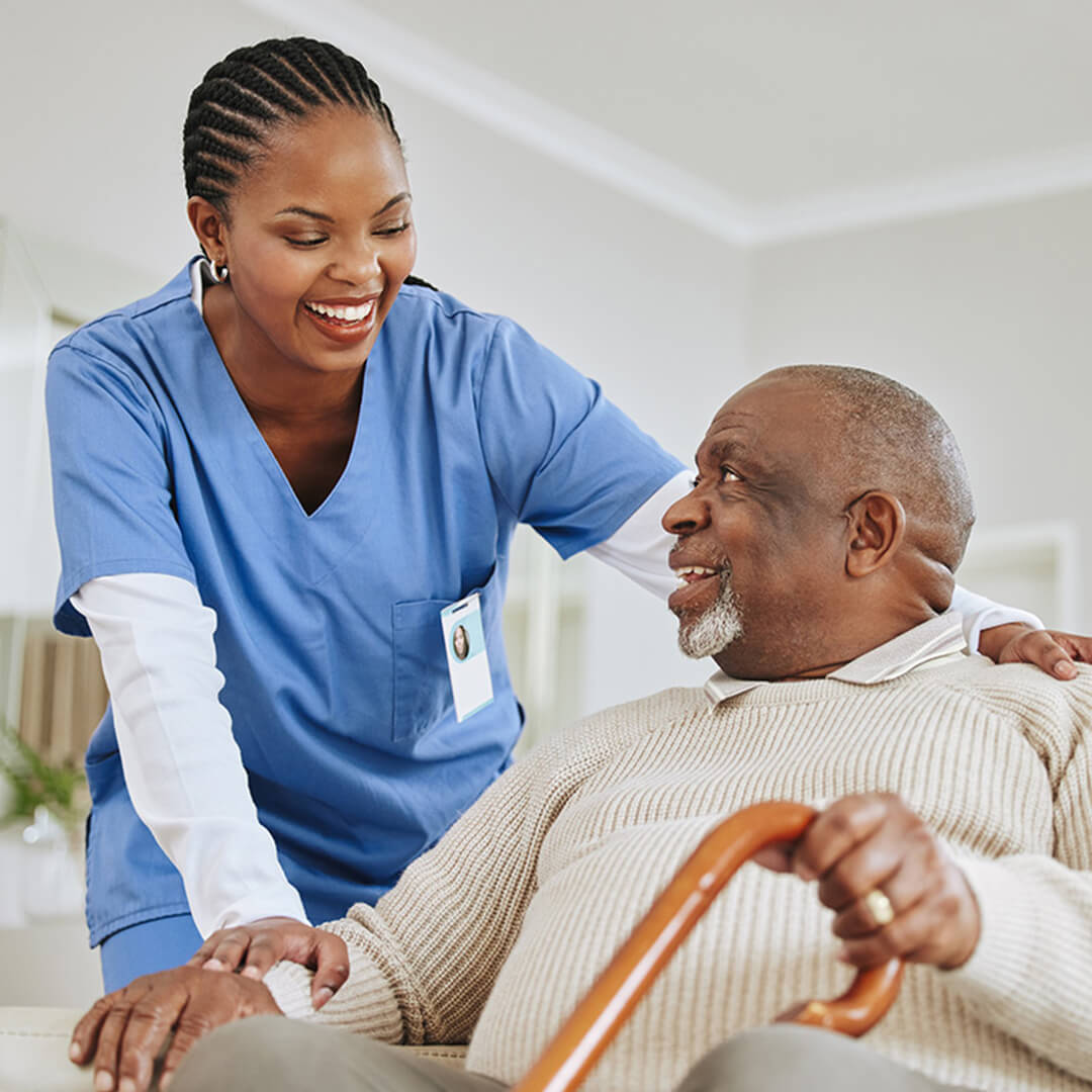 A nurse in scrubs comforts an elderly cancer patient