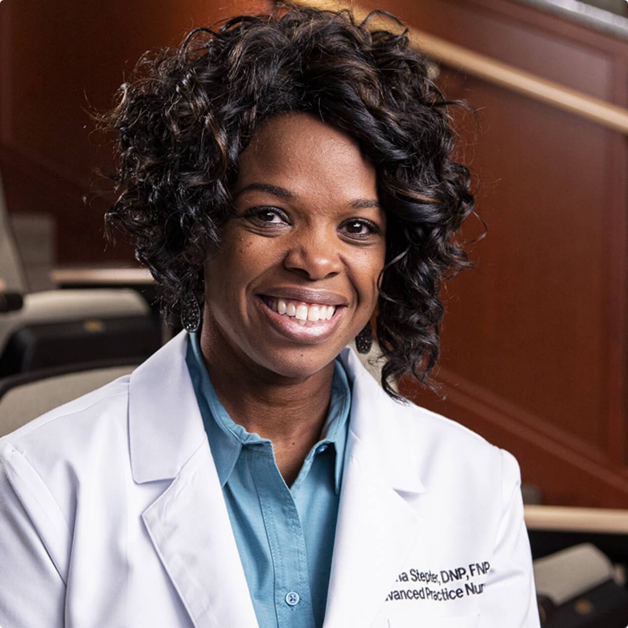 Clesheree Stepter, a smiling nurse practitioner in a white coat, sits in an auditorium-style clinic room, projecting confidence and compassion